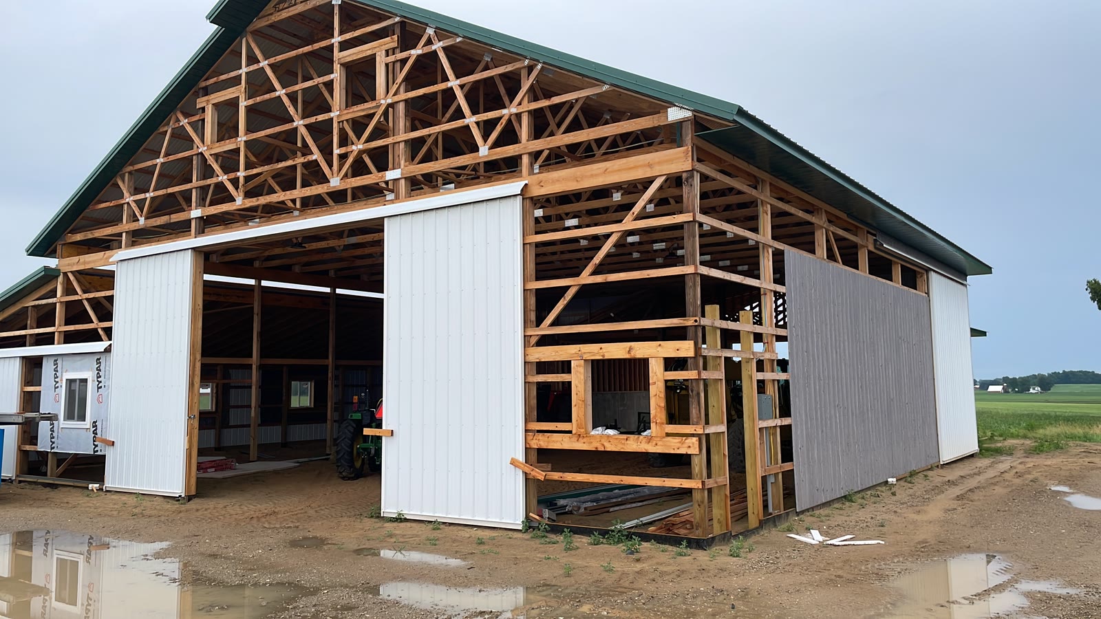 The barn mid-build — trusses set, sliding doors hung, tractor parked inside